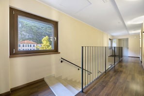 A hallway with a wooden floor, a glass staircase, and a window with a view of a building and trees.