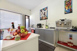 A modern kitchen with a coffee machine, a fruit display, and artwork on the walls.
