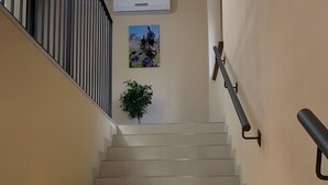 Eine Treppe mit Handlauf, eine Wandklimaanlage, ein gerahmtes Bild und ein Blumentopf.
