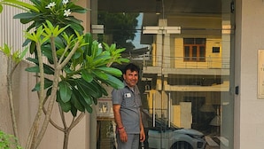 A man standing in front of a building entrance with large potted plants and a glass door. - Jaltara Stays @ Bapu Nagar, Jaipur 3BHK Apartment (Jaipur)