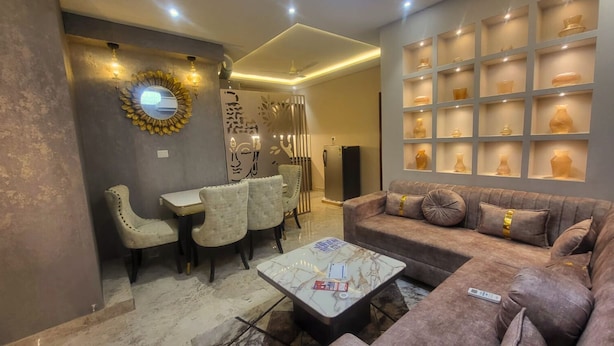 A modern living room with a sofa, coffee table, and chairs. There is a decorative wall with shelves displaying vases. - Jaltara Stays @ Bapu Nagar, Jaipur 3BHK Apartment (Jaipur)