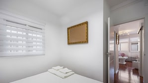 A bedroom with a bed, a window with blinds, a framed mirror, and a view into a bathroom. - La Justicia Apartment with Private Parking, Shared Terrace, Wi-Fi & Air Conditioning (Jerez de la Frontera)
