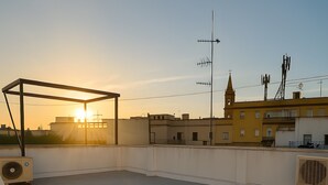 A rooftop terrace with a metal frame structure, air conditioning units, and a clear view of the sunset. - La Justicia Apartment with Private Parking, Shared Terrace, Wi-Fi & Air Conditioning (Jerez de la Frontera)
