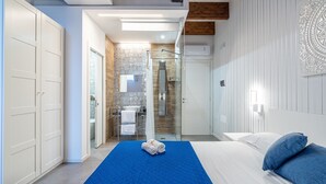 A hotel room with a bed, a bathroom with a shower, and a wardrobe. - Room 103 at 'Le Saline Rooms Marzamemi' – Wi-Fi and Air Conditioning (Marzamemi)