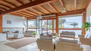 Un'ampia area interna con mobili in vimini, ampie finestre e soffitto in legno.