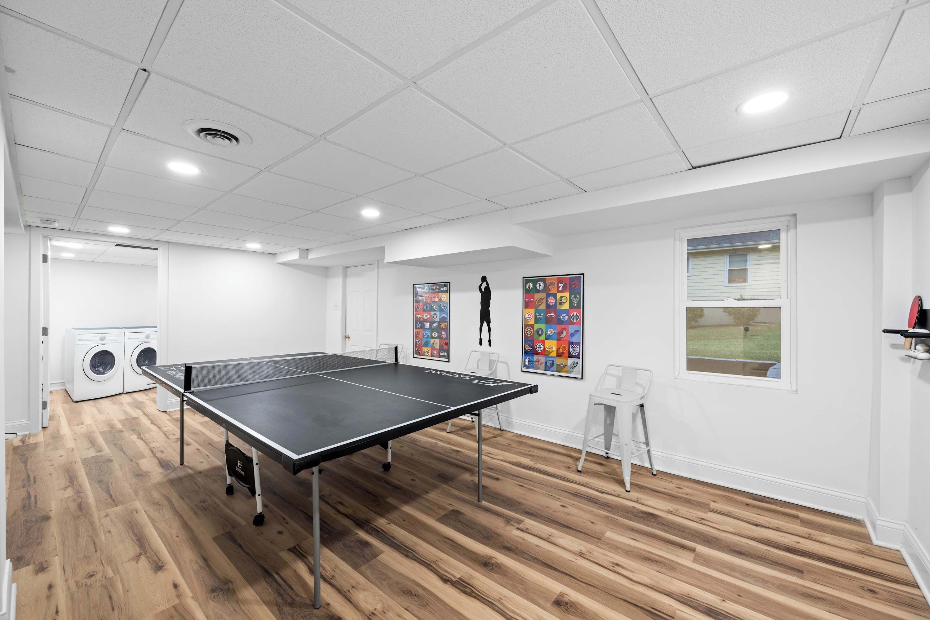 Una habitación con mesa de ping pong, lavadora y ventana con vista a un paisaje verde.