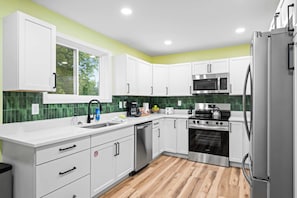 A modern kitchen with white cabinets, a stainless steel refrigerator, a microwave, an oven, and a dishwasher.