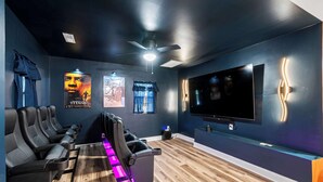 A modern home theater with dark walls, a large flat-screen TV, and a row of comfortable seating. - Movie Theater, Game room, 4BR near Spooky Nook (Hamilton)