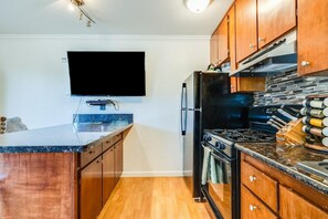 Een keuken met houten kastjes, een zwarte koelkast, een fornuis en een flatscreen televisie aan de muur.