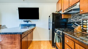 A modern kitchen with wooden cabinets, a black refrigerator, a stove, and a flat-screen TV mounted on the wall.