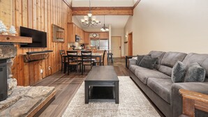 Een ruime woonkamer met een open haard, een bank, een eettafel met stoelen en een keuken op de achtergrond.