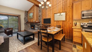 Een gezellige woonkamer met een open haard, houten wanden, een eethoek en een keuken met een accentmuur van steen.