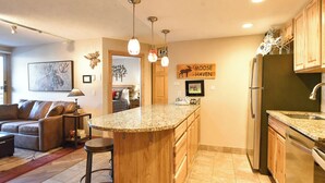 A kitchen with a central island, wooden cabinets, a refrigerator, and a dining area with a sofa and a coffee table.