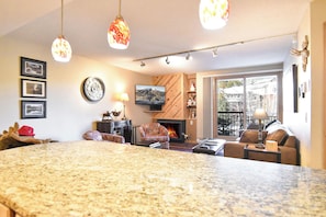 A spacious living area with a large granite island, a fireplace, comfortable seating, and a television mounted on the wall.