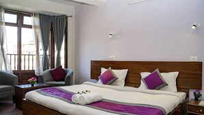 Habitación de hotel con una cama grande, dos sillones, una mesita con un florero y una mesita de noche.