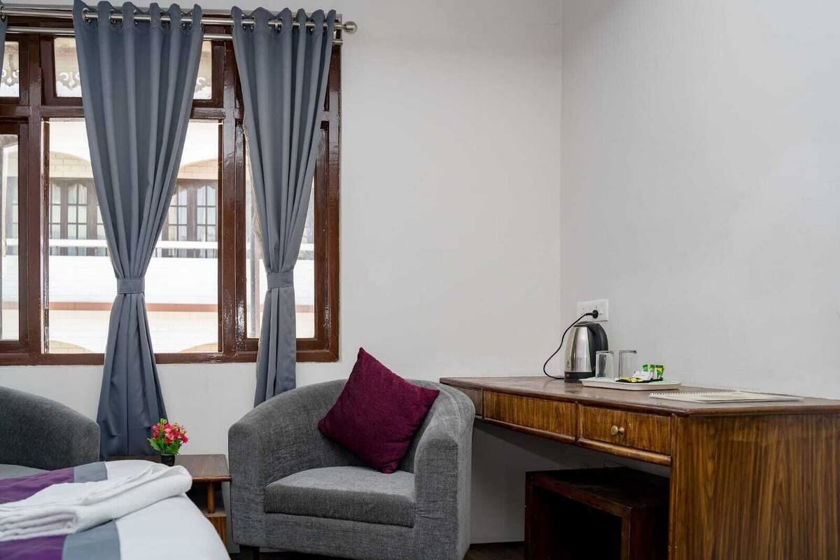 A hotel room with a grey sofa, a wooden desk, and a window with curtains.