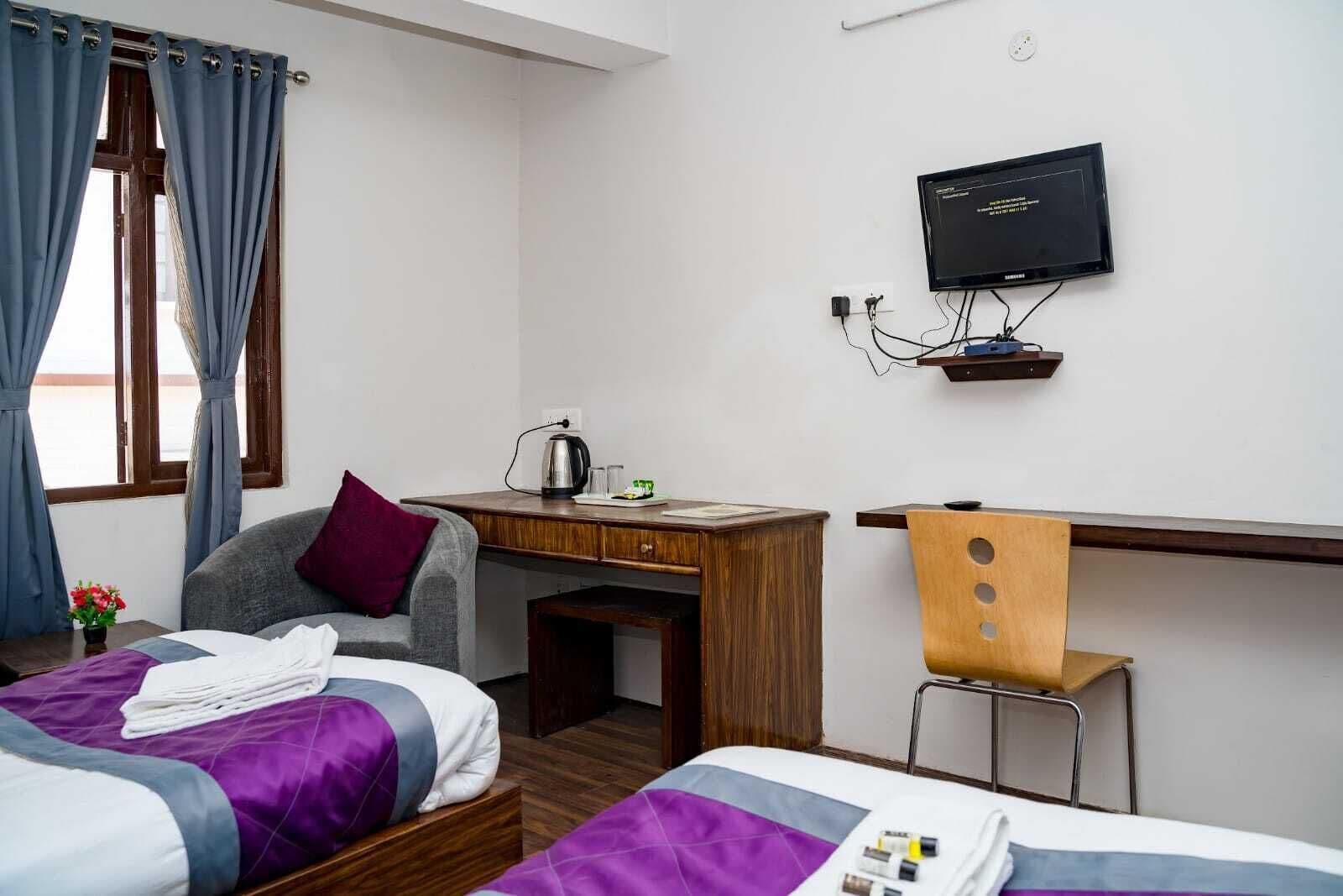 Habitación de hotel con dos camas, un escritorio, una silla, un televisor y una ventana con cortinas.