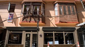 Un hotel con panadería y cafetería en la planta baja, un balcón con cortinas y un cono naranja cerrado con cadena.