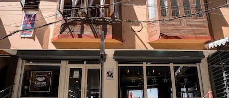 A hotel with a bakery and cafe on the ground floor, a balcony with curtains, and a chain-locked orange cone.