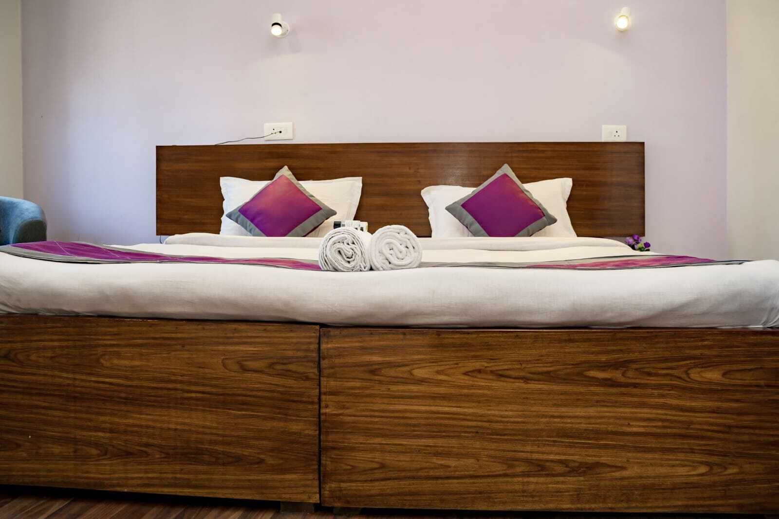 A neatly made bed with a wooden headboard, two pillows, and a rolled towel.