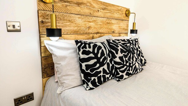 Ein Bett mit Holz-Kopfteil, zwei Nachttischlampen und gemusterten Kissen.