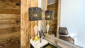 Ein Badezimmer mit Holzwand, Marmorwaschbecken, zwei Lampen mit gemusterten Schirmen, einem Spiegel und einem Stuhl.