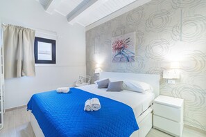 Une chambre d’hôtel avec un lit, une table de chevet, une lampe, une fenêtre avec des rideaux et un mur orné d’un tableau représentant des fleurs.