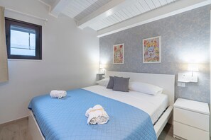 A hotel room with a bed, two wall-mounted lamps, a window, and two framed artworks.