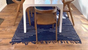 Un coin repas avec une table blanche, six chaises en bois, un tapis bleu tissé et une suspension.