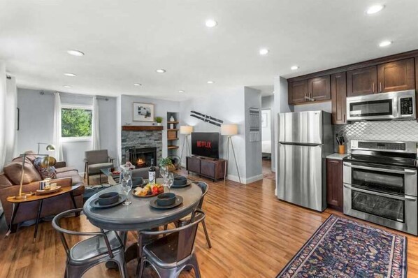 A modern kitchen with stainless steel appliances, a dining area with a round table, and a living space with a fireplace.