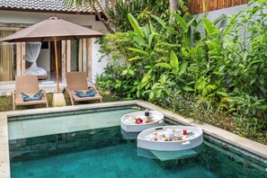 A pool area with lounge chairs, a dining setup on floating platforms, and lush greenery. - Balima Villa  (Seminyak)