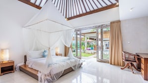Een ruime slaapkamer met een groot bed, een houten bureau en uitzicht op de tuin.