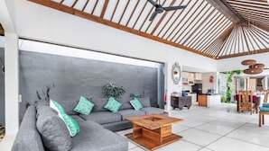 Een ruime woonkamer met een grijze bank, een houten salontafel en een plafondventilator.