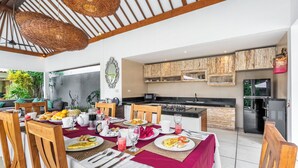 Een eetgedeelte met een ontbijt gedekte tafel, houten stoelen en uitzicht op de keuken en buitenruimte.