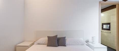 A modern bedroom with a bed, two bedside tables, a TV, and towels.