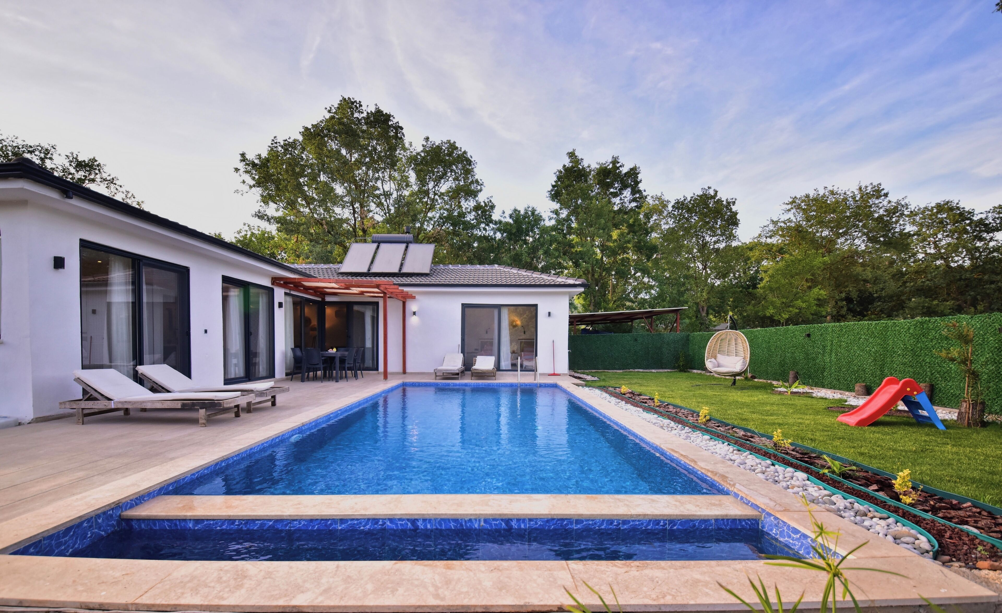 A modern house with a swimming pool, a patio with lounge chairs, and a slide.