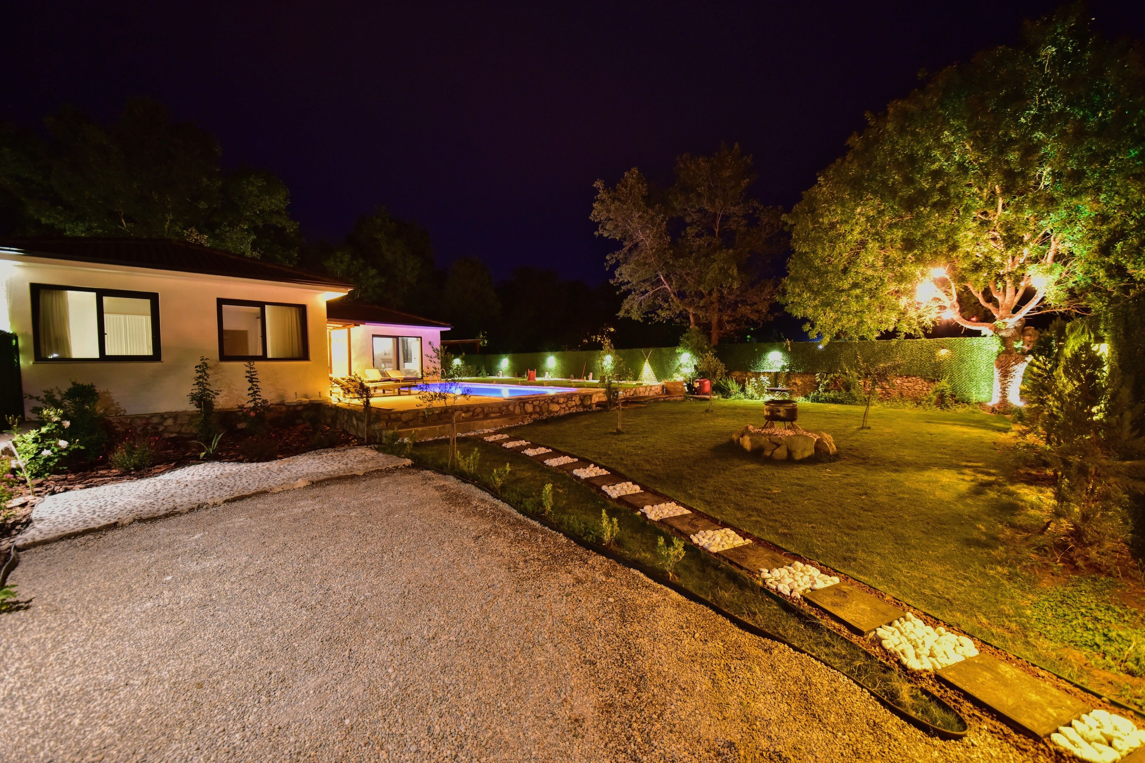 A well-lit outdoor area with a swimming pool, a stone pathway, and a small water feature.