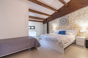 A bedroom with a bed, a bedside table, a nightstand, a wooden ceiling, and a patterned wall.
