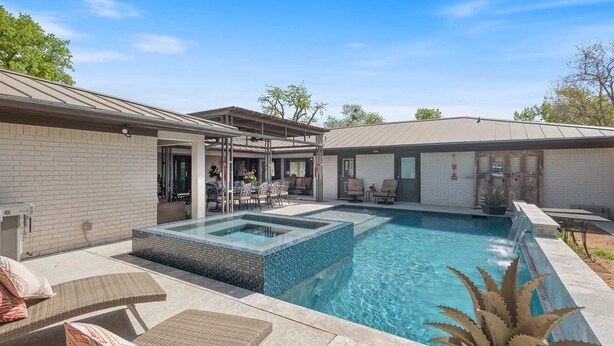 Un patio trasero con piscina, una parrilla y mobiliario exterior.