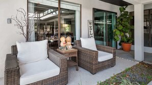 Un patio con mobiliario de mimbre, una mesa pequeña con adornos y una planta grande en maceta.