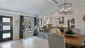 Una cocina moderna con armarios blancos, un comedor con mesa y sillas de madera, y una araña.