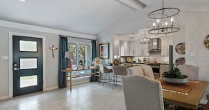 A modern kitchen with white cabinets, a dining area with a wooden table and chairs, and a chandelier.