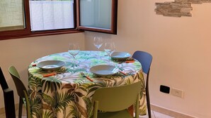 A dining area with a round table set for four, chairs, a window with a view of greenery, and a stone wall decoration.
