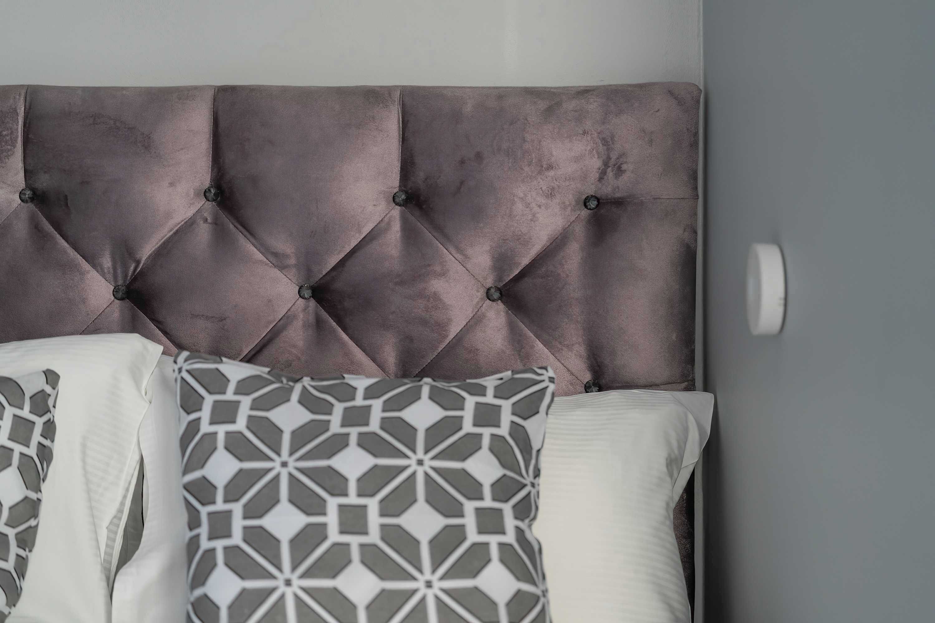 A bed with a tufted headboard, patterned pillows, and a plain wall.