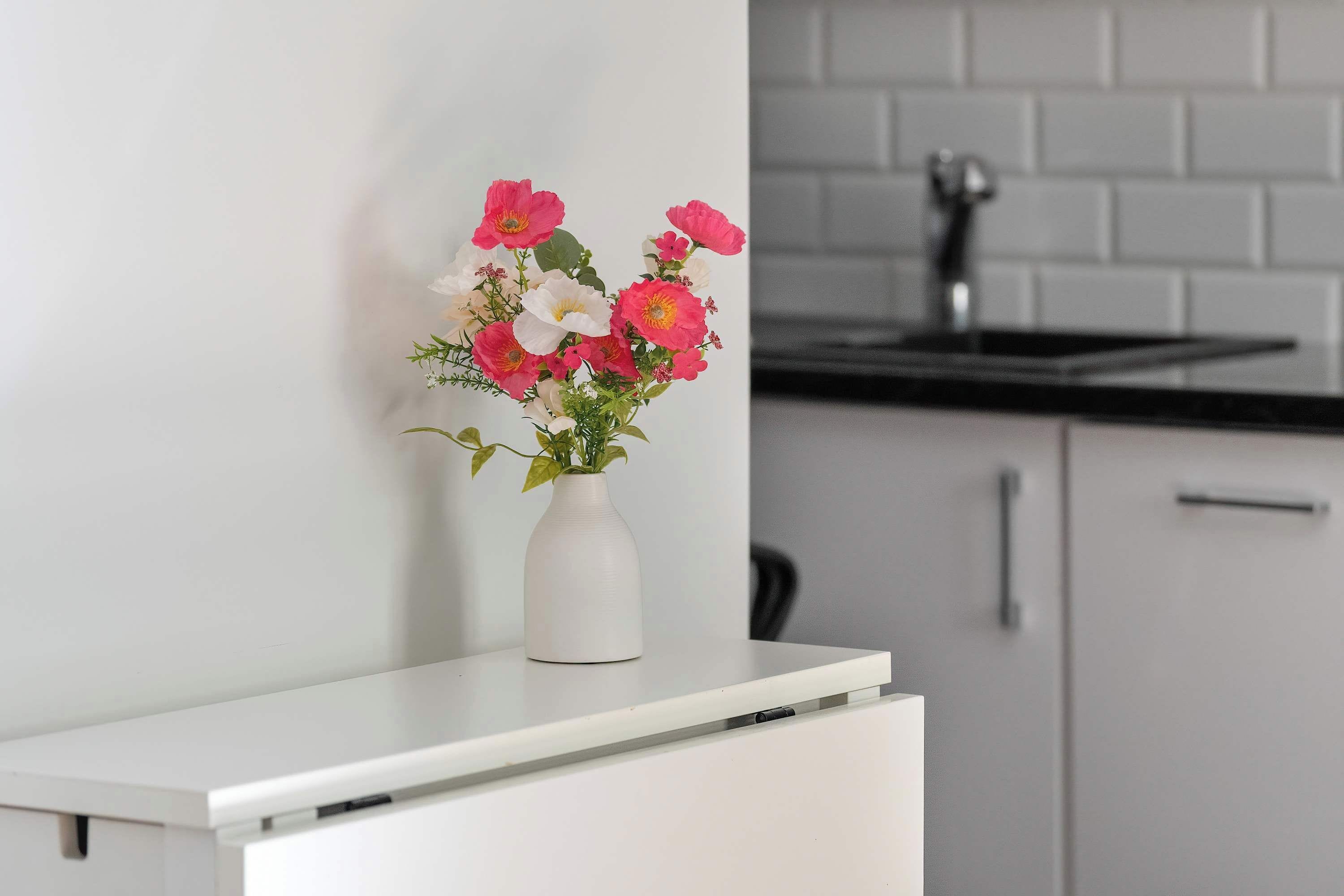 A white cabinet with a white vase containing pink and white flowers.