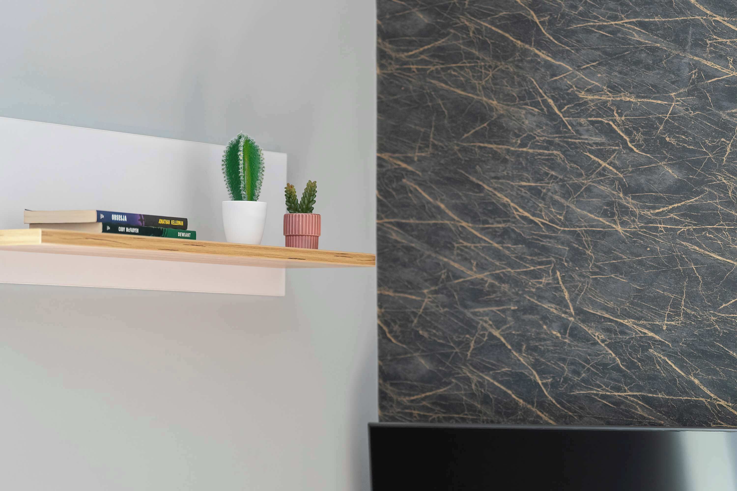 A modern interior with a marble wall, a shelf with books and plants, and a flat-screen TV.