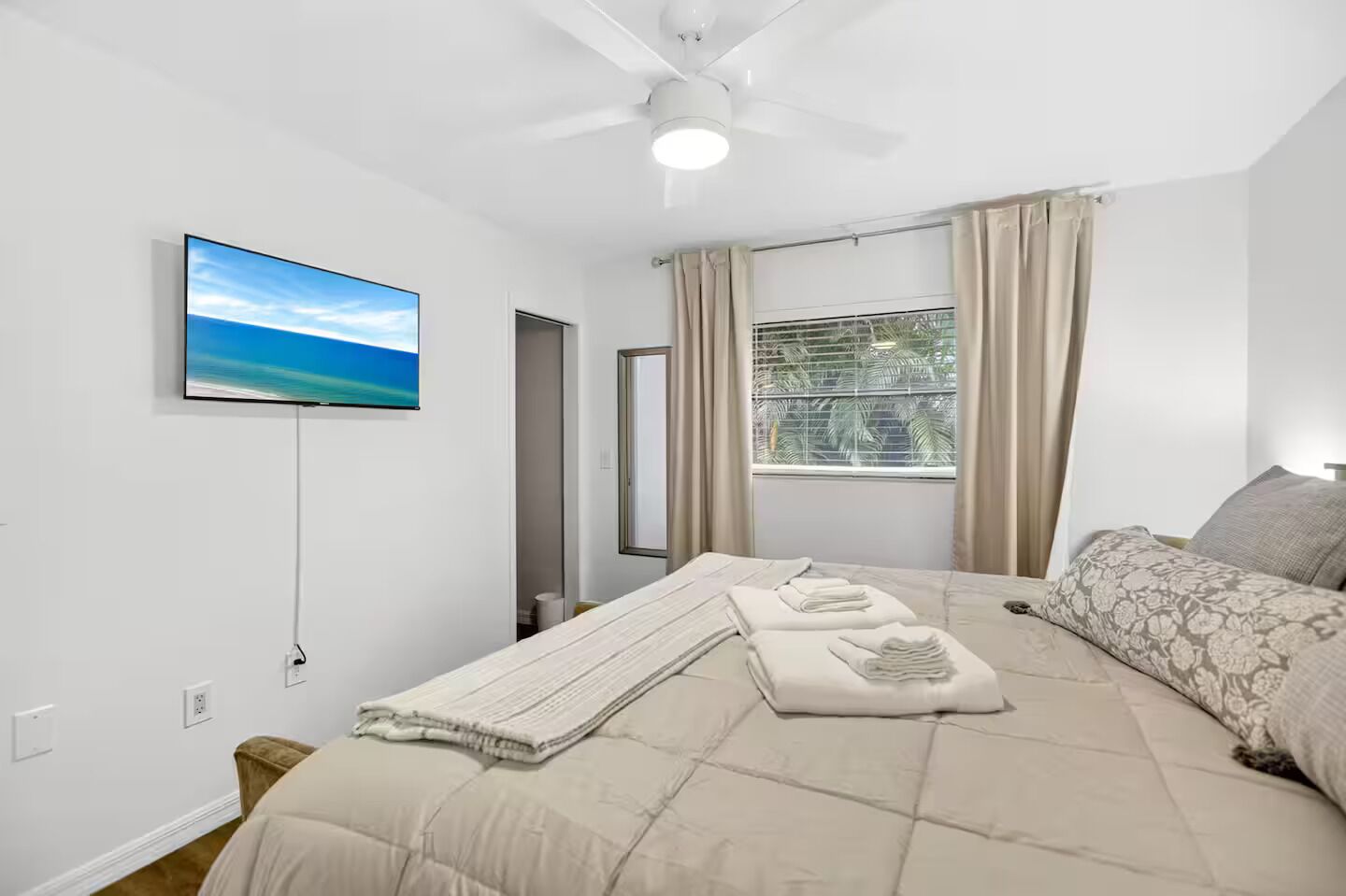 Ein Schlafzimmer mit Bett, Fernseher, Deckenventilator und einem Fenster mit Vorhängen.
