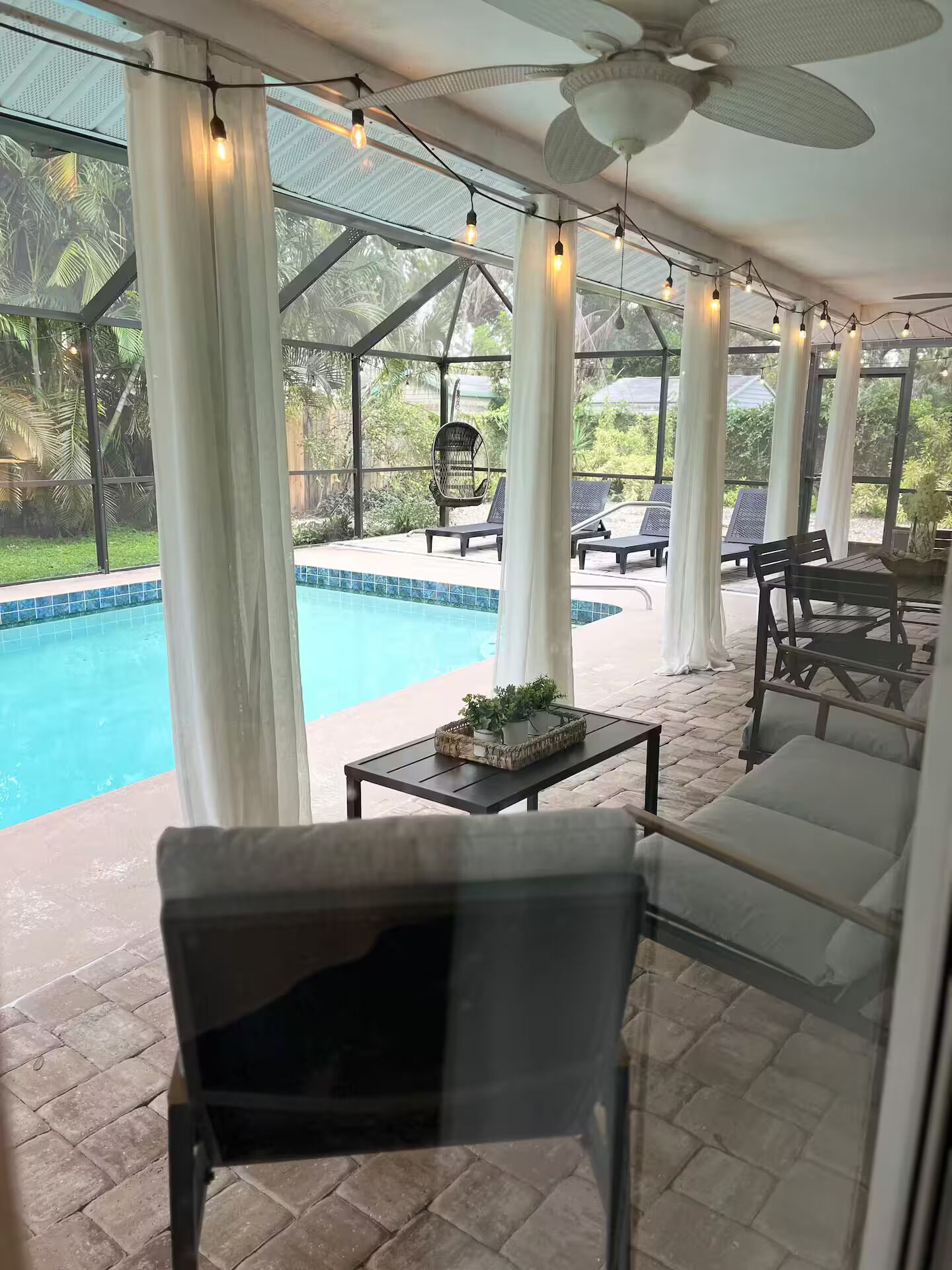 A covered outdoor area with a pool, lounge chairs, and a ceiling fan.