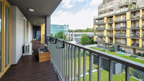 Ein Balkon mit Holzboden, Blick auf benachbarte Gebäude und einem wolkenlosen Himmel.