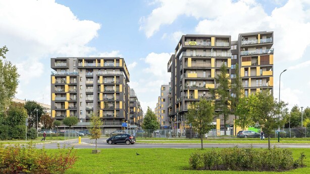 Ein modernes Mehrfamilienhaus mit mehreren Balkonen, einem Parkplatz und einem Grünanlagen im Vordergrund.